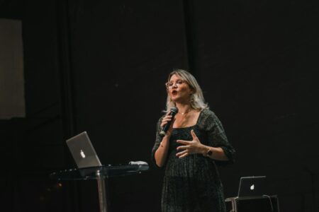 Female speaker addressing audience at podium with microphone during public speaking event