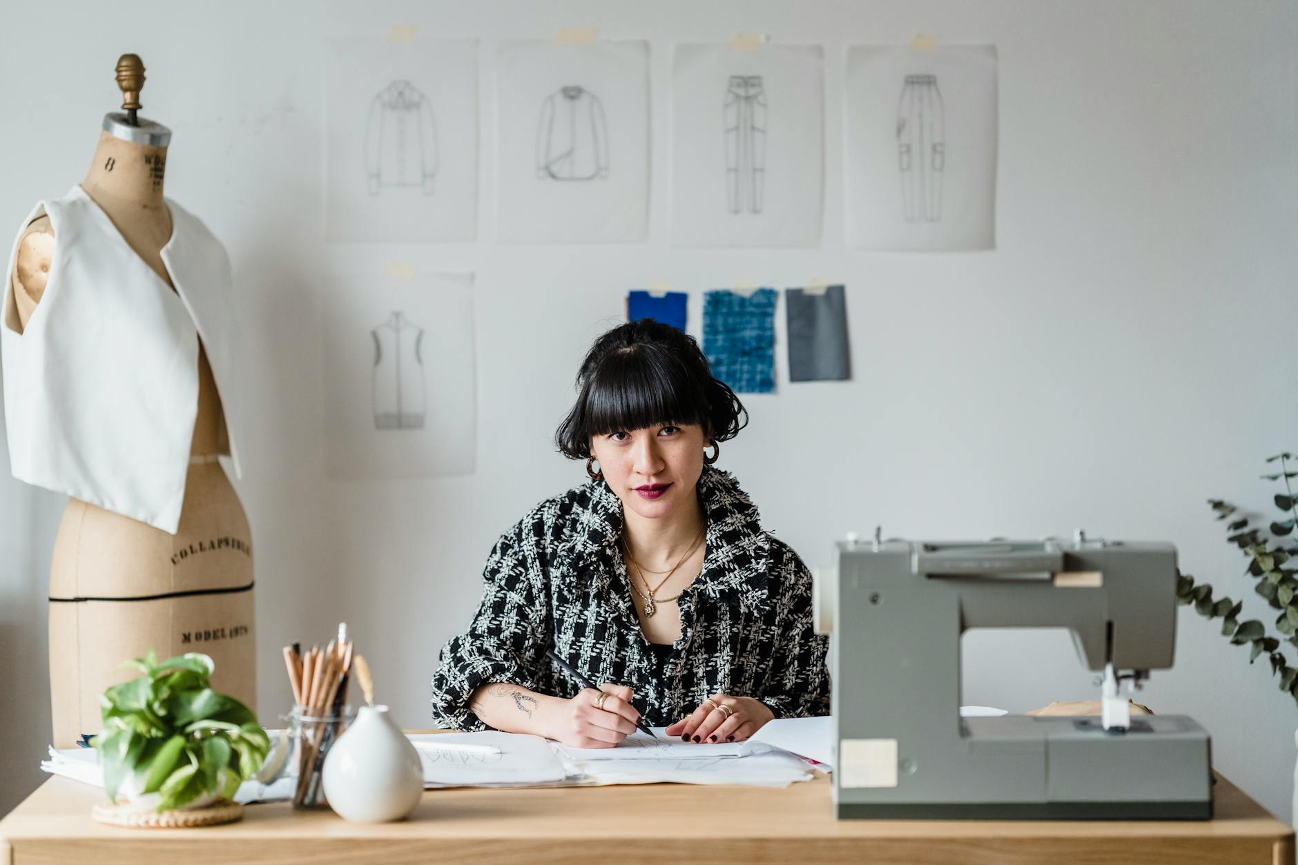 Fashion designer's workspace with sketches, fabric samples, and sewing materials spread across a modern studio table