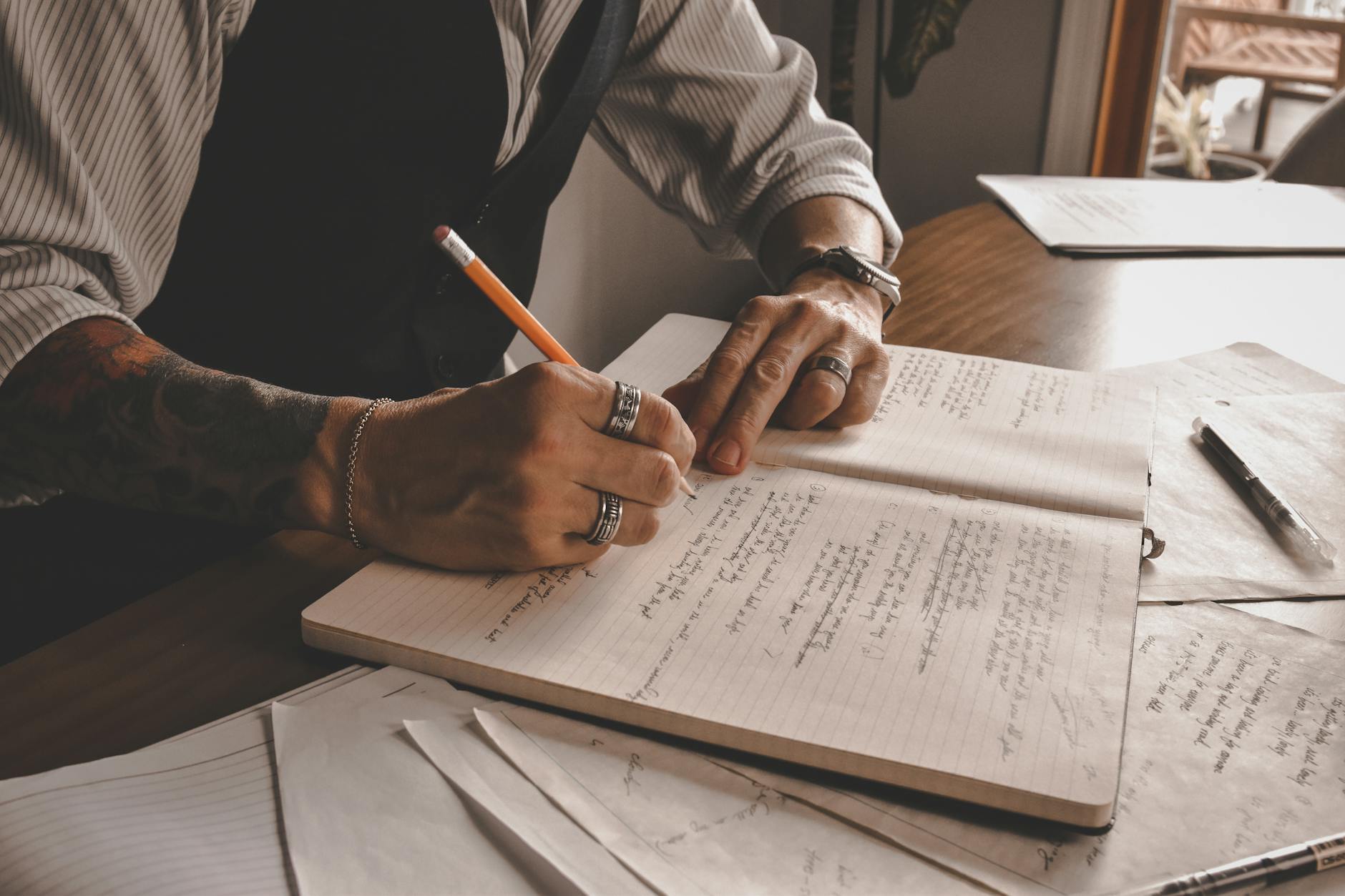 Person writing in notebook at wooden desk with laptop nearby