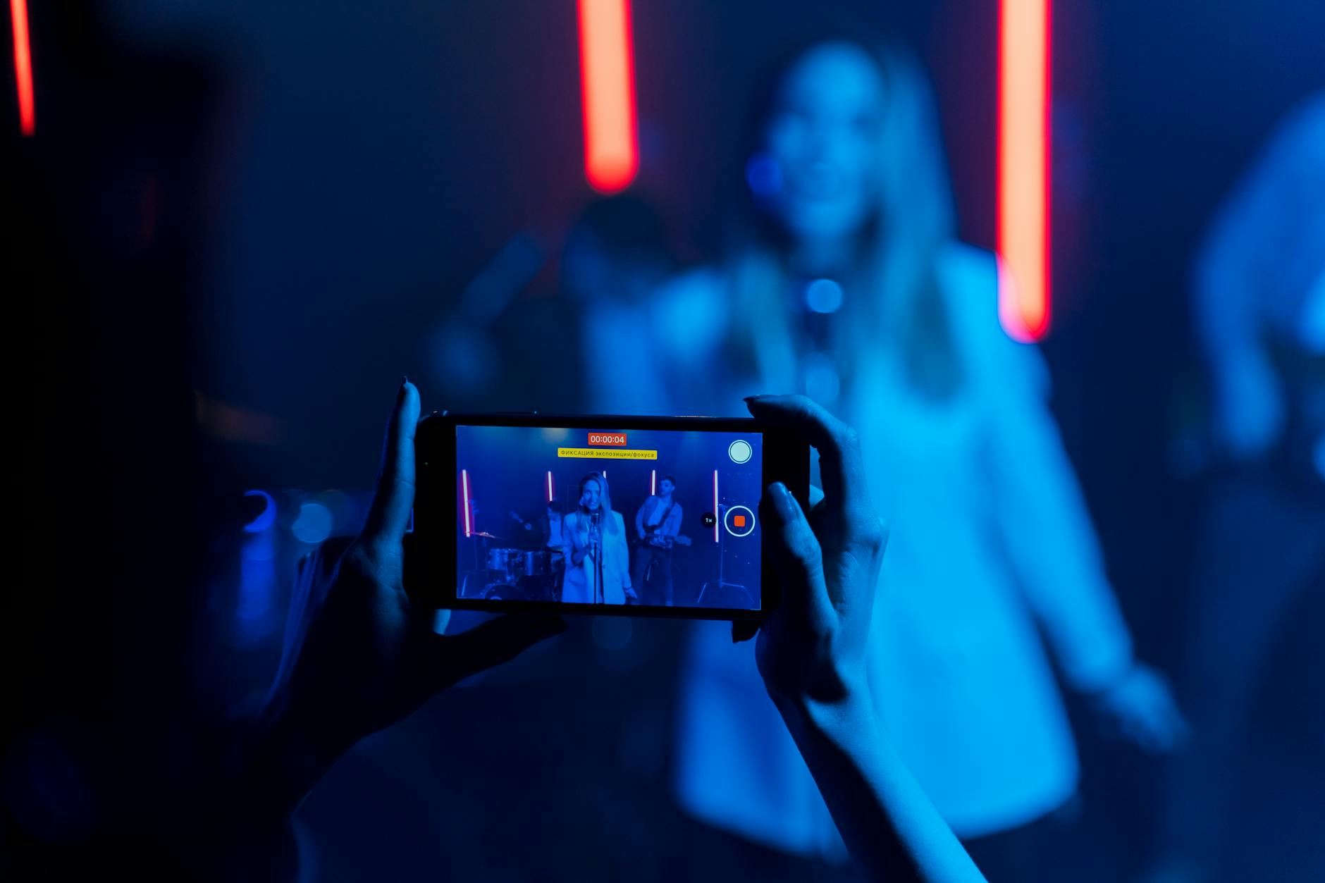 Hand holding smartphone recording live concert performance with stage lights in background