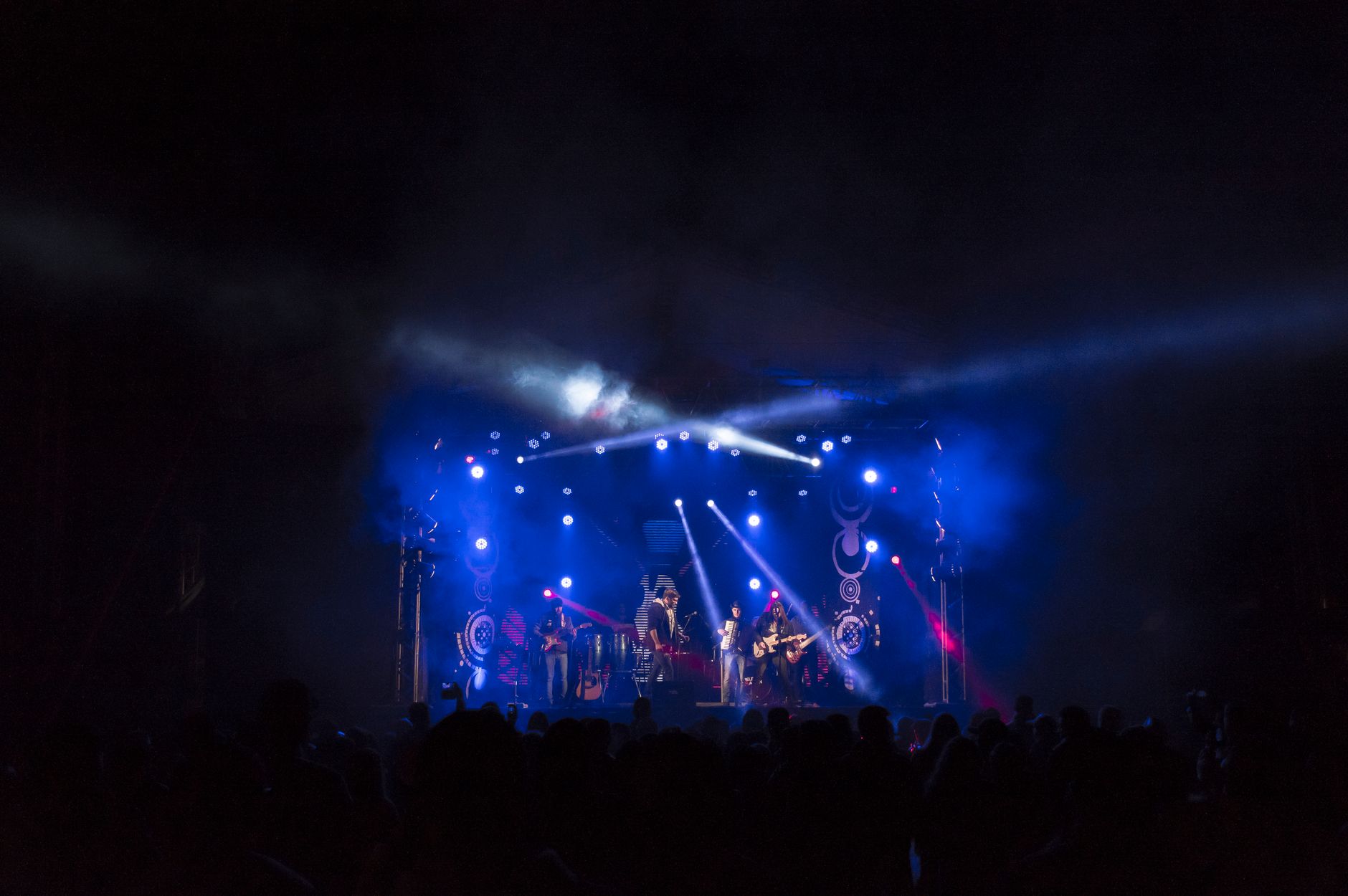 A performer on a brightly lit pop concert stage facing a large audience