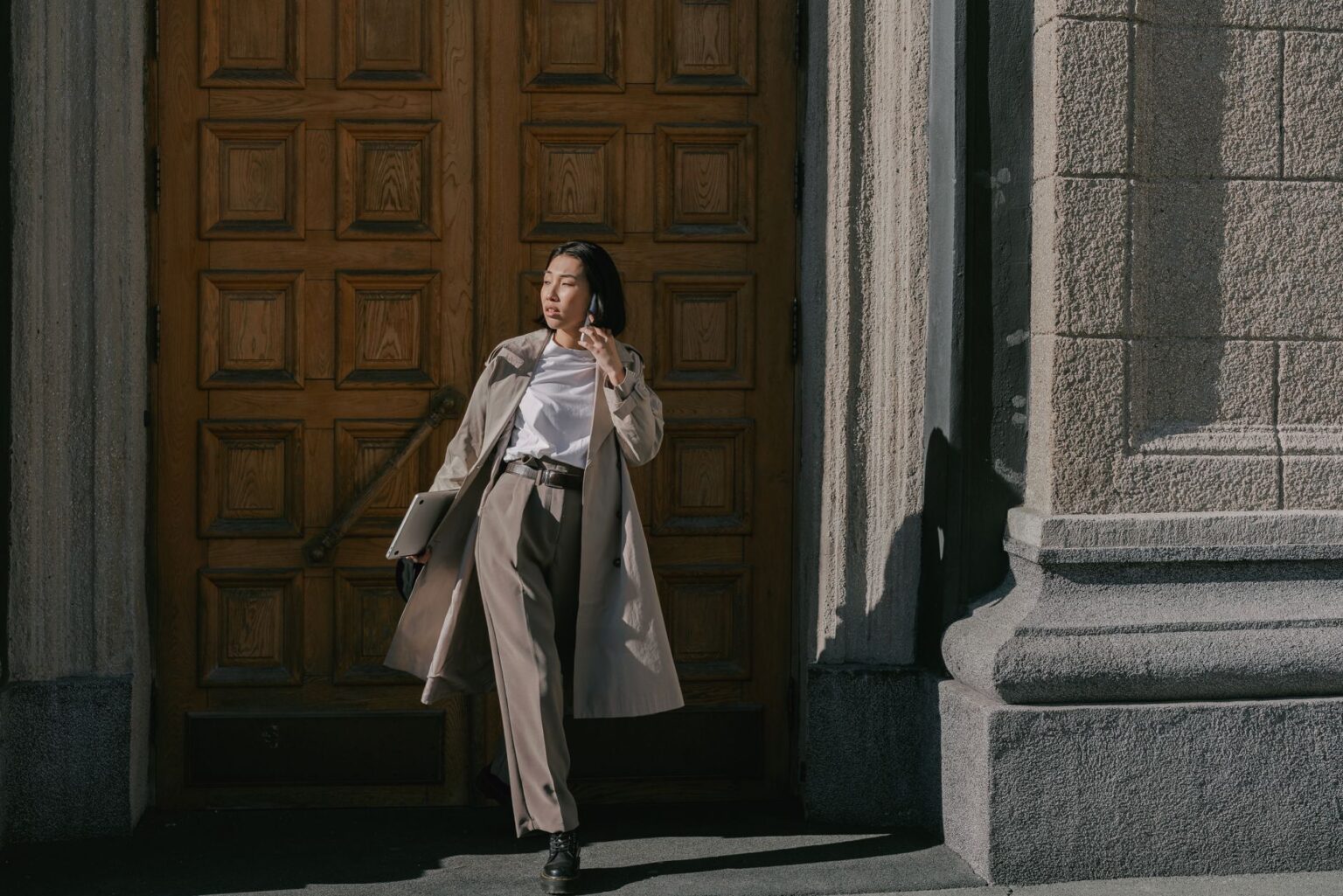 Toteme’s Belted Trench Is Quietly Edging Out the Wrap Coat Woman wearing a structured belted trench coat on a city street