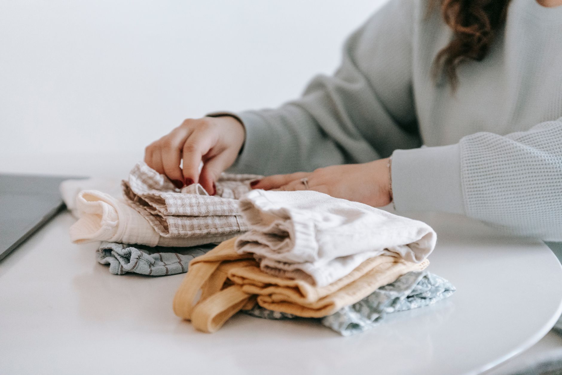 Neatly folded neutral-colored sweaters on a shelf, representing considered wardrobe basics