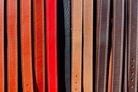 The Slim Belt Is Quietly Reclaiming the Waist From Minimalism A narrow cognac leather belt with simple brass buckle laid flat on a neutral surface