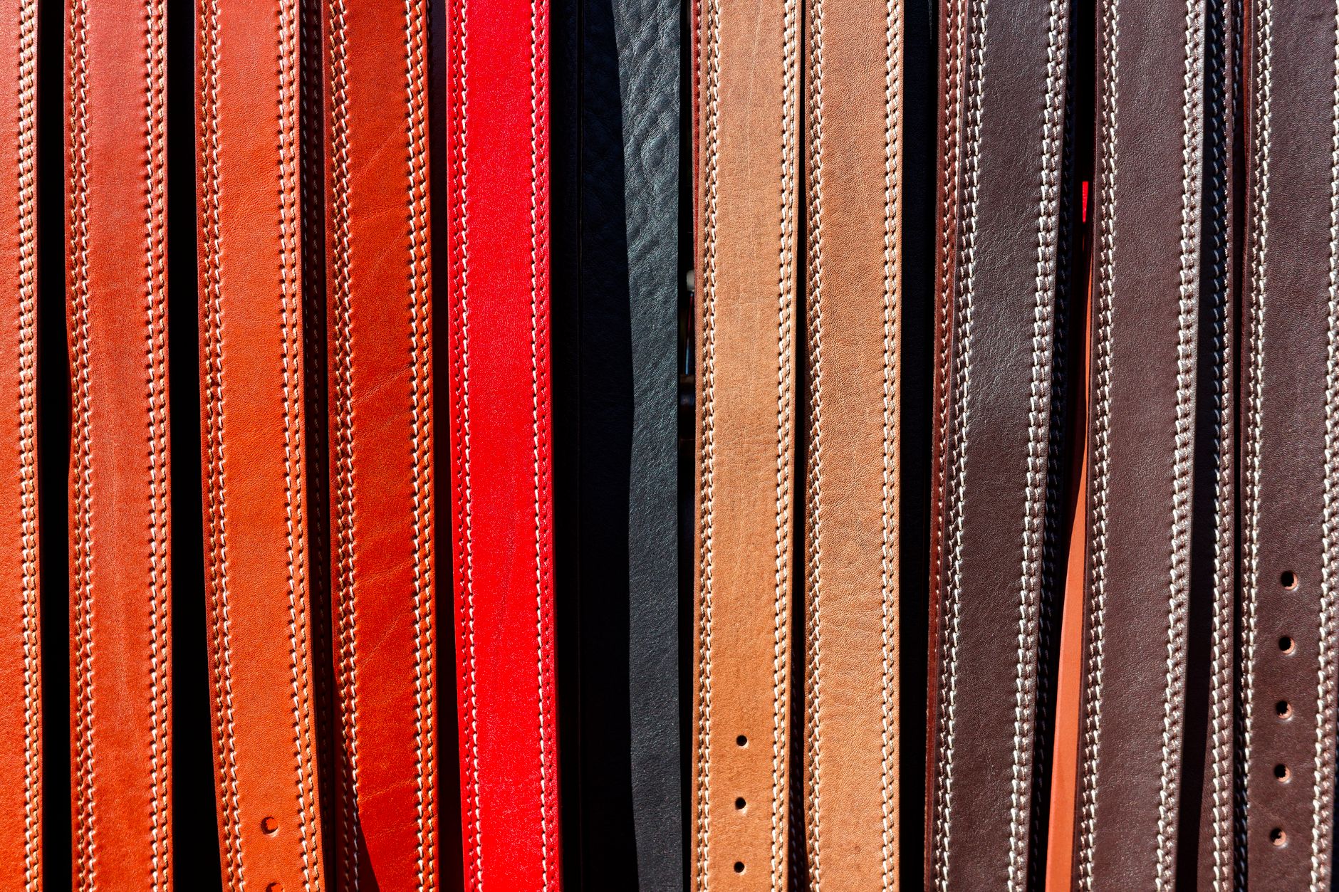 A narrow cognac leather belt with simple brass buckle laid flat on a neutral surface