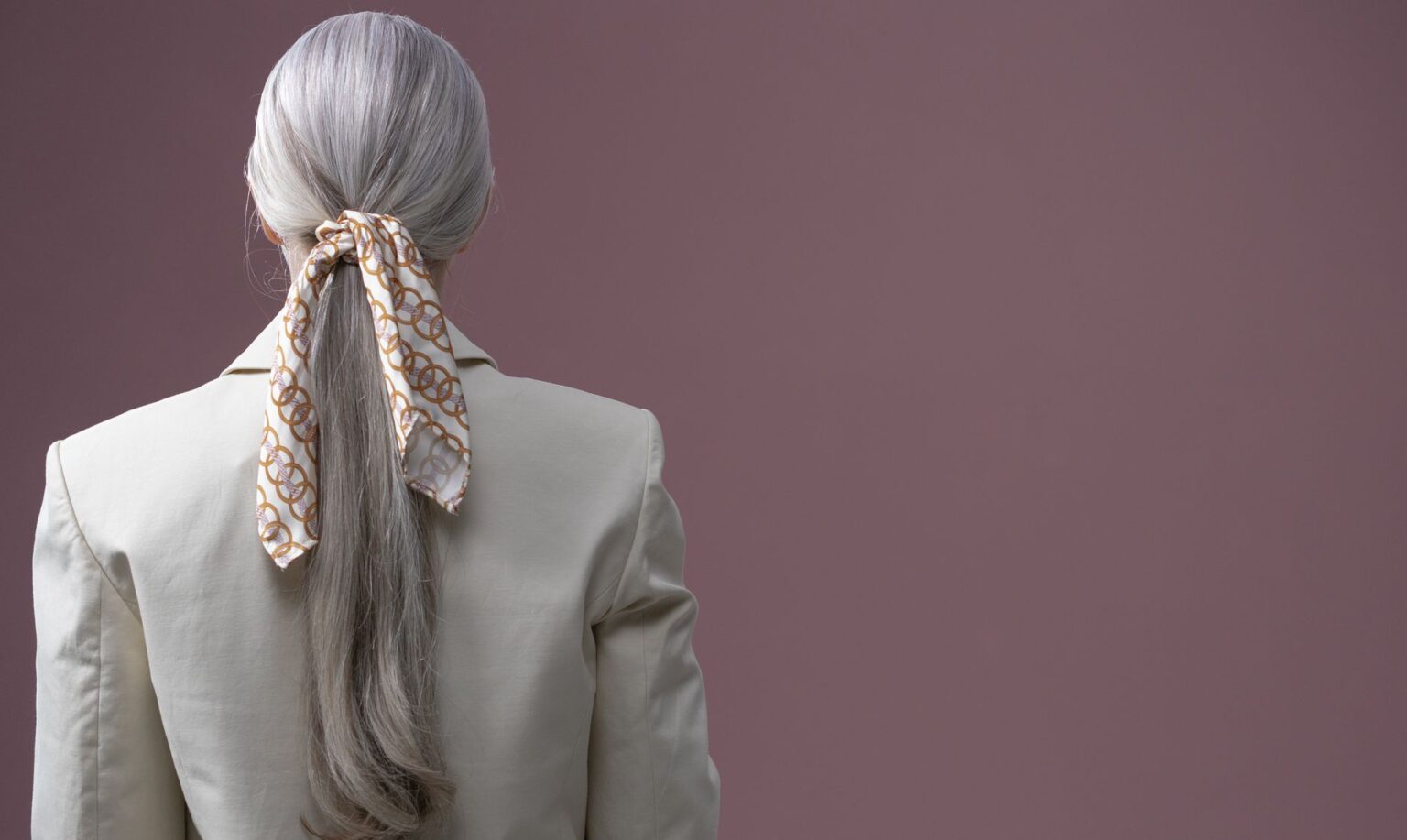 The Slim Scarf Is Quietly Edging Out the Statement Necklace A narrow silk scarf draped loosely around a woman's neck over a simple outfit