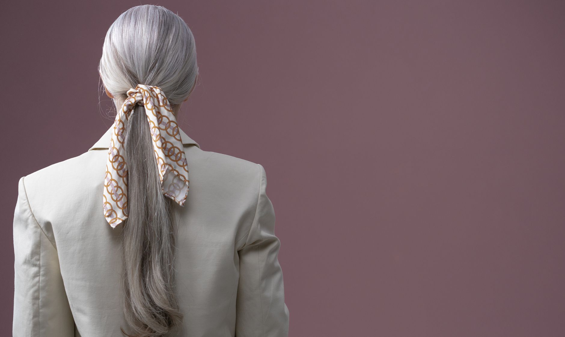 A narrow silk scarf draped loosely around a woman's neck over a simple outfit