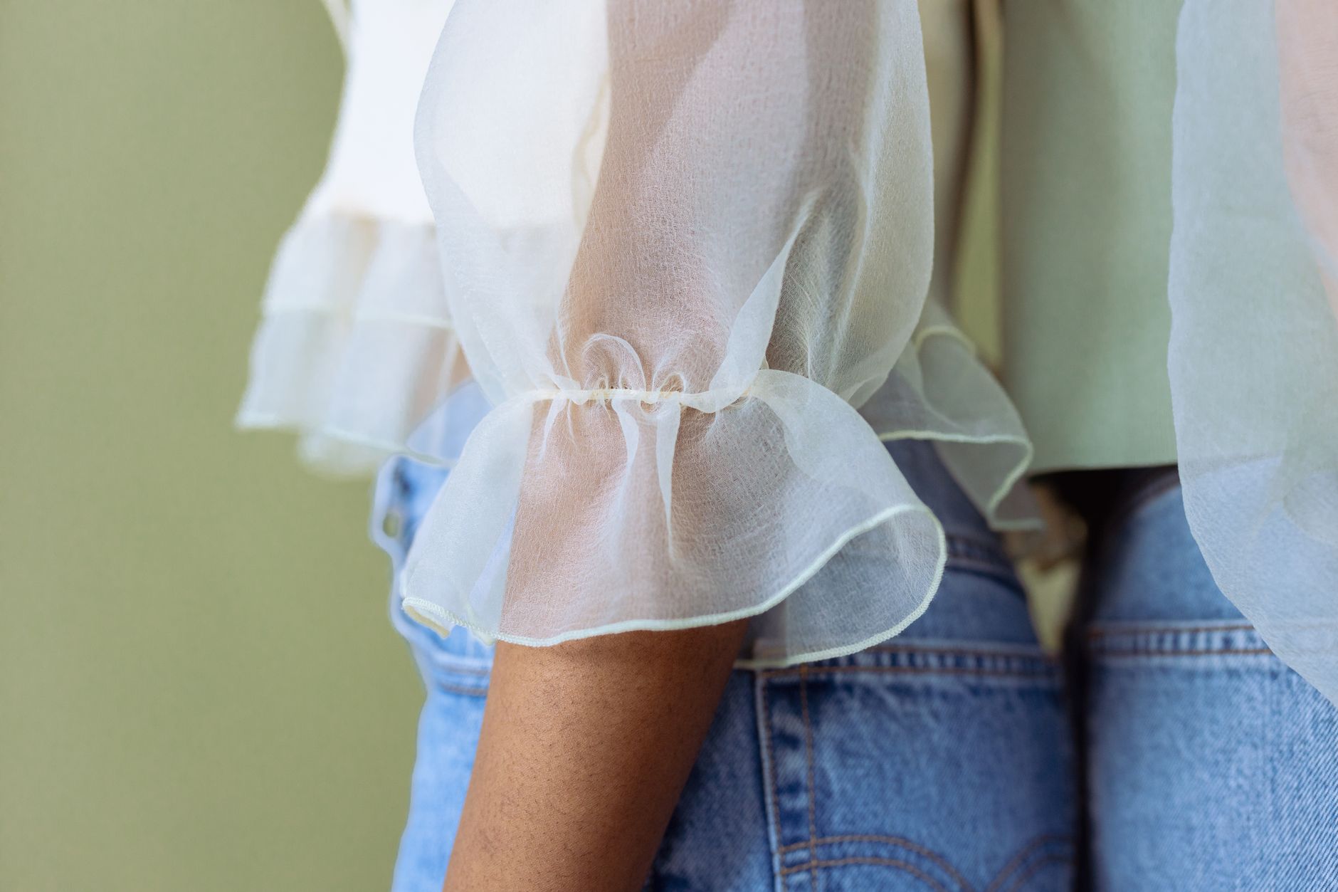 Close-up of gathered fabric detail at the shoulder of a light linen blouse