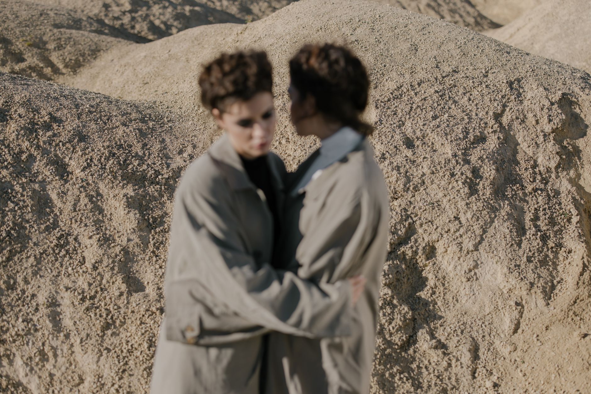 An editorial-style fashion photograph featuring neutral-toned outerwear against a clean background