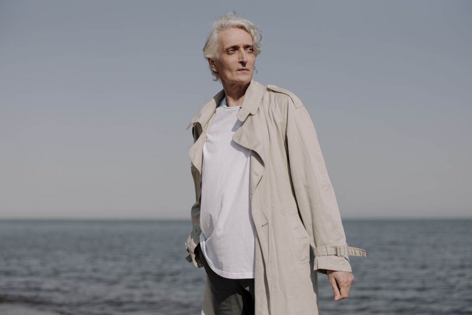 The Broderie Anglaise Trench Is Quietly Edging Out the Cotton Mac A white structured trench coat displayed on a model against a neutral background