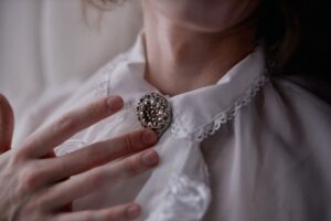 The Broderie Anglaise Collar Is Quietly Edging Out the Statement Earring Close-up of a white broderie anglaise collar against a dark knit sweater