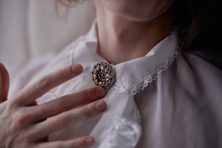 The Broderie Anglaise Collar Is Quietly Edging Out the Statement Earring Close-up of a white broderie anglaise collar against a dark knit sweater