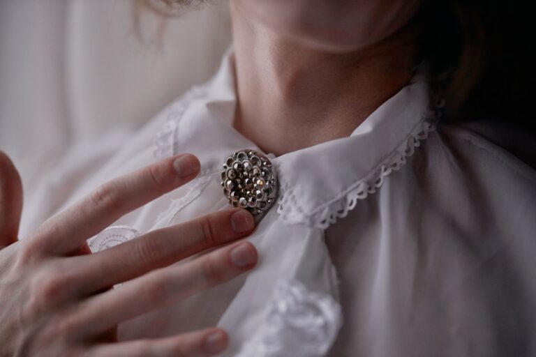 The Broderie Anglaise Collar Is Quietly Edging Out the Statement Earring Close-up of a white broderie anglaise collar against a dark knit sweater
