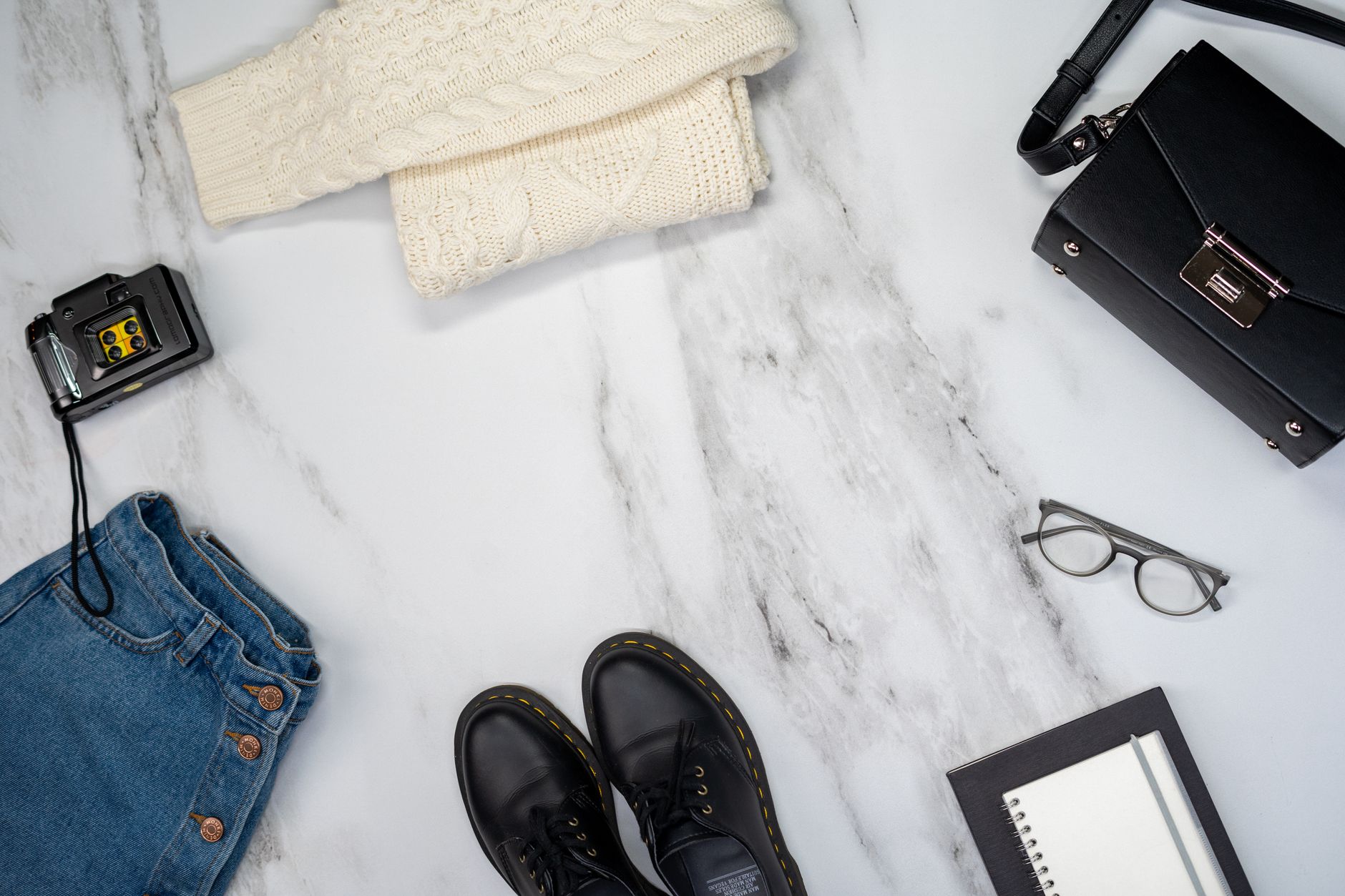 A flat lay of neutral wardrobe pieces including a white eyelet blouse and simple accessories