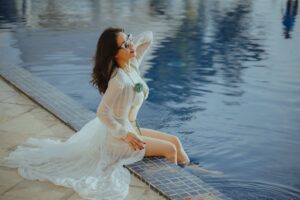 The Broderie Anglaise Swimsuit Is Quietly Edging Out the Printed Bikini Woman wearing a white textured swimsuit beside a bright outdoor pool