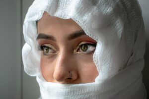 The Broderie Anglaise Headscarf Is Quietly Edging Out the Silk Square Scarf Woman wearing a white broderie anglaise headscarf tied loosely around her head