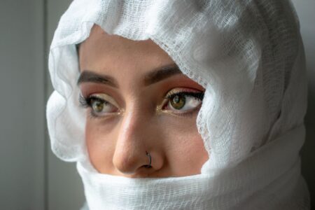 The Broderie Anglaise Headscarf Is Quietly Edging Out the Silk Square Scarf Woman wearing a white broderie anglaise headscarf tied loosely around her head