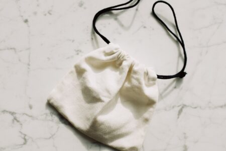 The Broderie Anglaise Bag Is Quietly Edging Out the Straw Clutch A white broderie anglaise fabric bag with eyelet embroidery detail on a light background