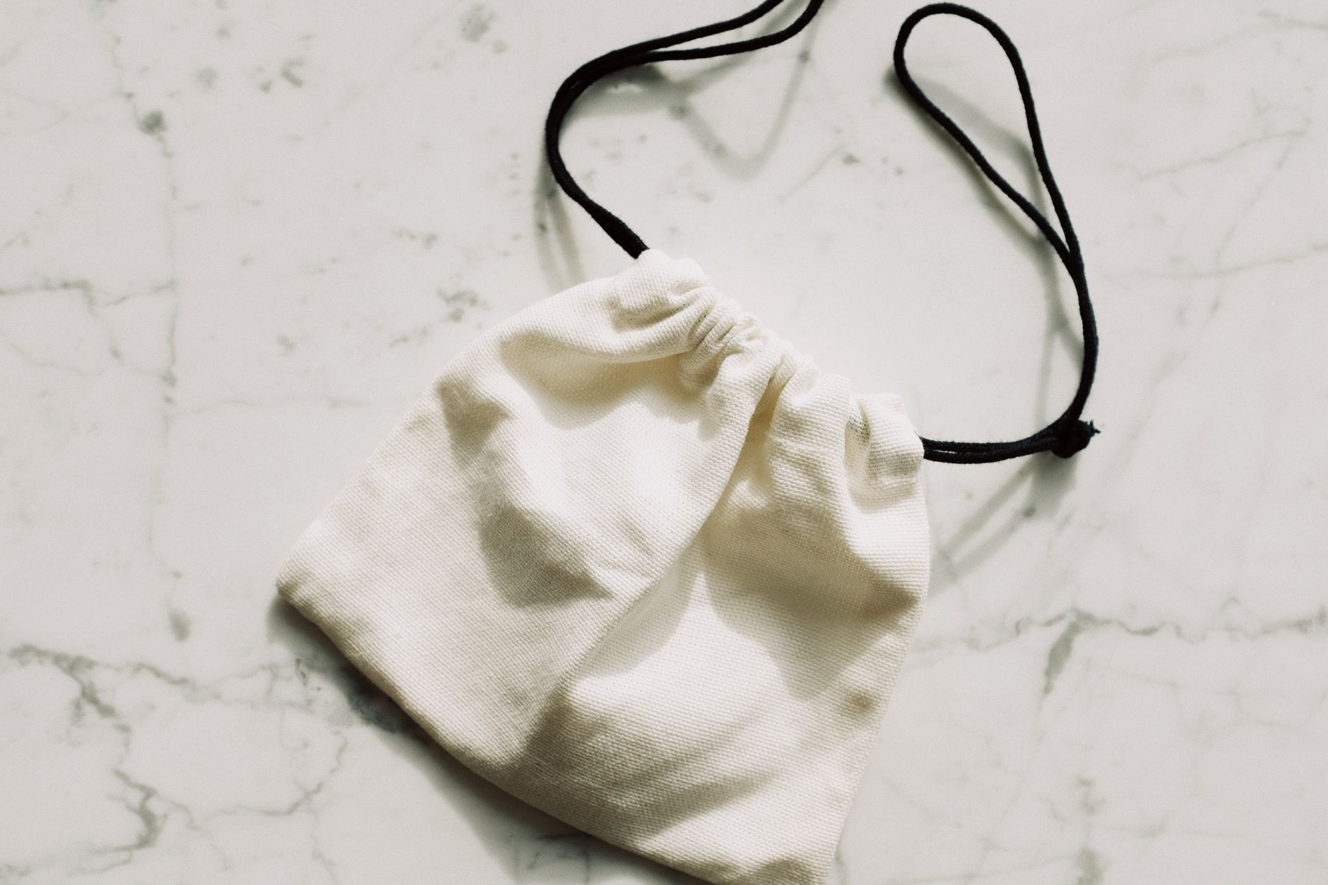 A white broderie anglaise fabric bag with eyelet embroidery detail on a light background