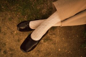 The Broderie Anglaise Flat Is Quietly Edging Out the Ballet Pump A pair of delicate white flat shoes with embroidered eyelet detailing on a light background